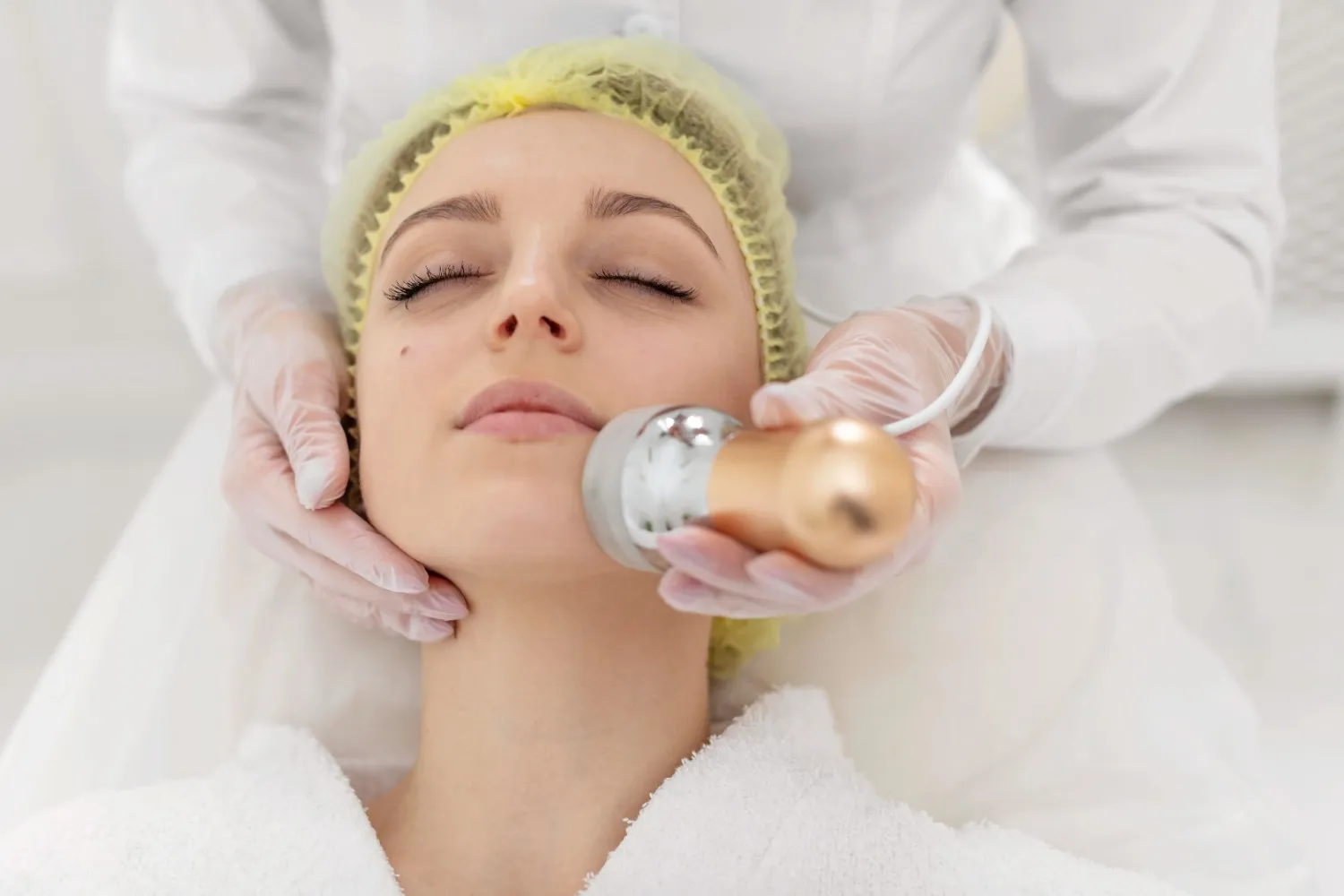 A woman receiving a cosmetic face treatment with a handheld device, commonly used in liposuction and nano fat rejuvenation procedures.